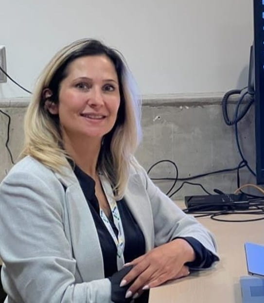 Dr April Khademi sitting at a desk with a laptop and a large monitor showing cells