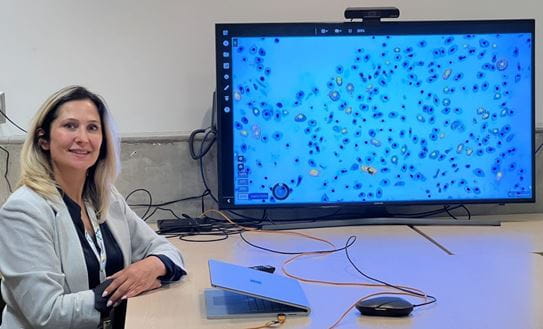 April Khademi, Ph. D., assise à un bureau devant un portable et un moniteur de grande taille montrant des cellules