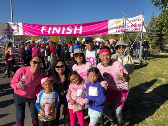 Vivian et sa famille posant devant la bannière de la ligne d’arrivée de la Course à la vie CIBC 2022 de la Société canadienne du cancer