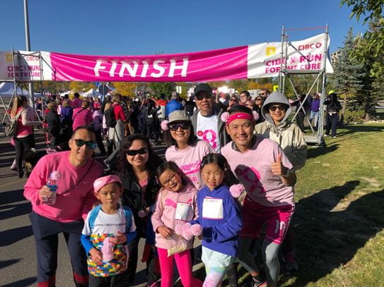 Vivian and her family posing in front of the finish line banner at the Canadian Cancer Society CIBC Run for the Cure