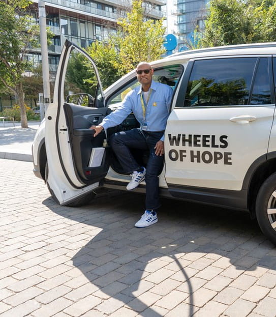 James assis au siège conducteur d'une voiture Wheels of Hope avec la portière ouverte.
