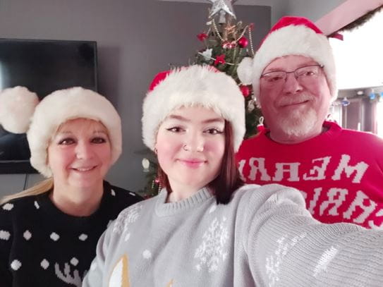 Hailey et ses parents, souriant à la caméra et portant des chapeaux de père Noël.