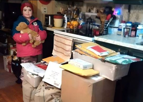 Hailey, avec un chien en peluche dans les bras, se tenant debout à côté de boîtes remplies de cartes de Noël.