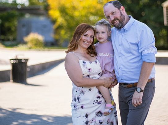 Natalie Lipschultz, carrying her daughter, stands next to her husband in a park.