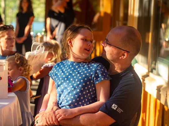 Inara, sitting in her father’s lap with other families at Camp Goodtimes.