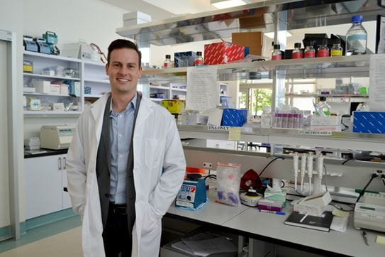 Le chercheur Alexander Wyatt, Ph. D., dans son laboratoire, portant un sarrau et souriant pour la photo