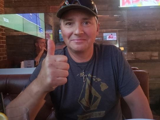 Sébastien sitting at a restaurant table, smiling and giving a thumbs up