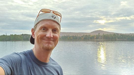 Stephen Medhurst standing in front of a lake and smiling at the camera