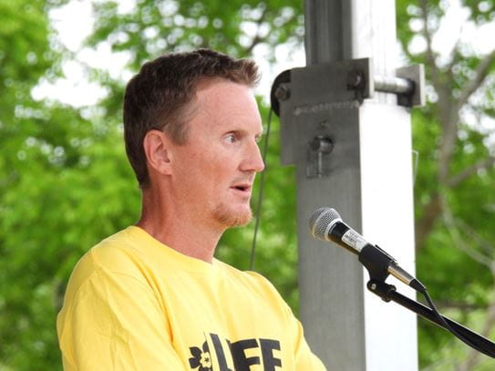 Stephen Medhurst in front of a microphone, speaking at a Relay For Life event and wearing a Relay T-shirt