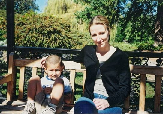 A young Amory sitting on a bench with Rochana. They are surrounded by trees.