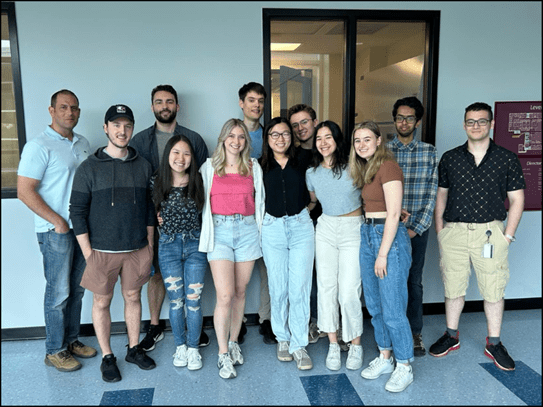 Le chercheur Anthony Rullo, Ph. D., debout près de 11 jeunes membres d’une équipe dans un couloir.