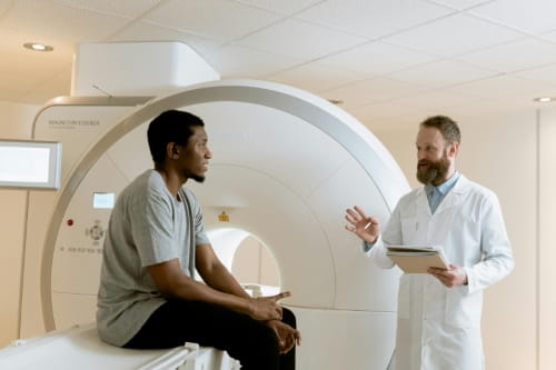 A doctor speaking to a person sitting on an MRI machine.