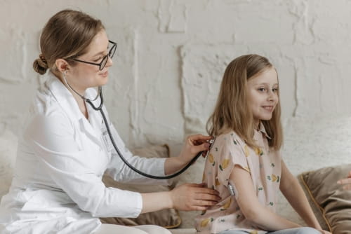 A doctor holding a stethoscope to a child’s back.