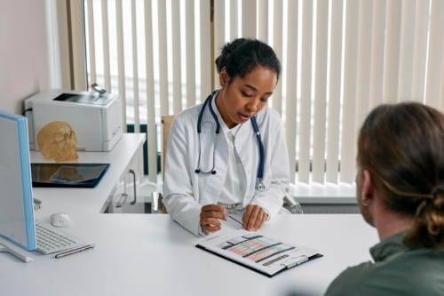 A doctor sitting with a person in their office and looking down at a chart.