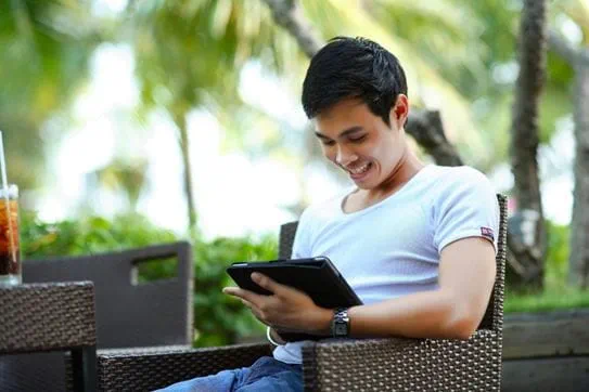 A person sitting outside and smiling at a tablet.