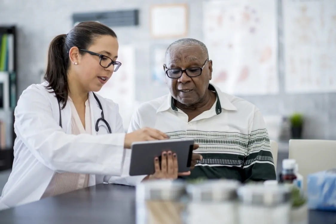 A doctor points to a tablet device while a patient looks on.