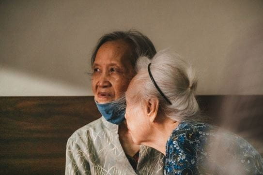 Two people sitting together. One of them wearing a mask around their chin.
