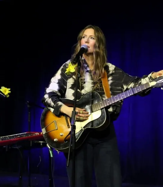 BEYRIES standing on a stage holding a guitar and singing into a microphone.