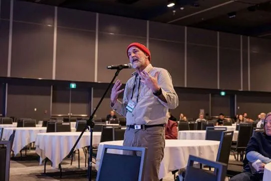 Angus speaking into a microphone in a conference room at an event.