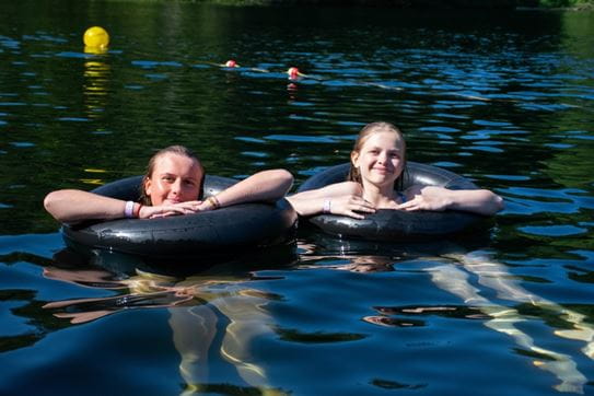 Two campers floating in the lake in inner tubes and smiling at the camera.