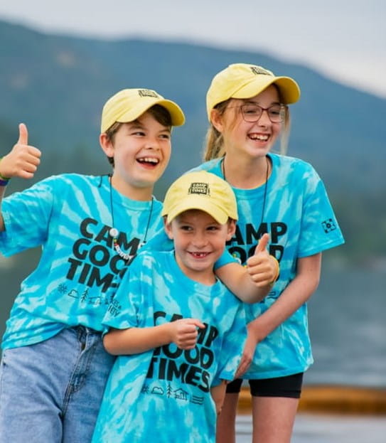 Trois enfants souriants, portant des t-shirts et des casquettes assortis aux couleurs du Camp Goodtimes.