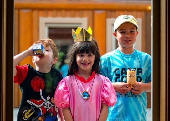 (left to right): a child drinking juice, a child wearing a crown and smiling, a child wearing a hat and holding a toy.