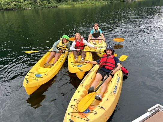 Four kids in their own kayaks holding paddles and wearing lifejackets.