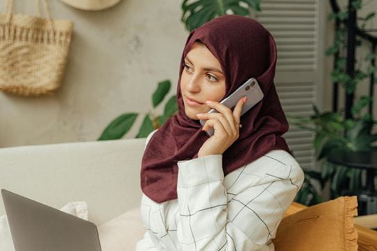 Une personne assise sur un canapé avec son téléphone cellulaire à l’oreille.