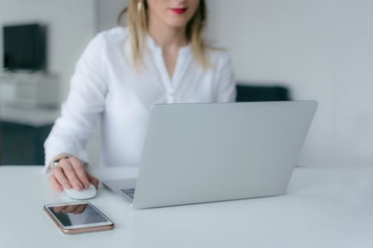 A person sitting at a desk working on a laptop with their hand on a mouse.