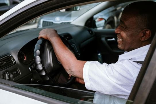 A person sitting in the driver’s seat of a car with their hand on the wheel and smiling.