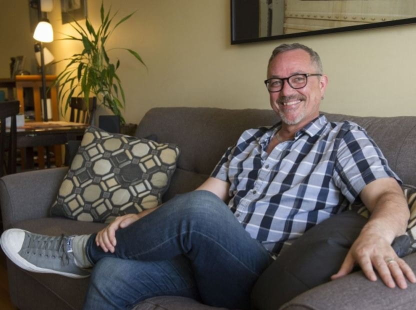 Patrick Gilmore souriant sur un canapé, les jambes croisées.