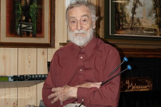 James Miller looking at the camera with his arms crossed, holding part of a musical instrument.