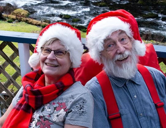 James Miller and Gladys Suderman smiling and wearing Santa hats in front of a river.