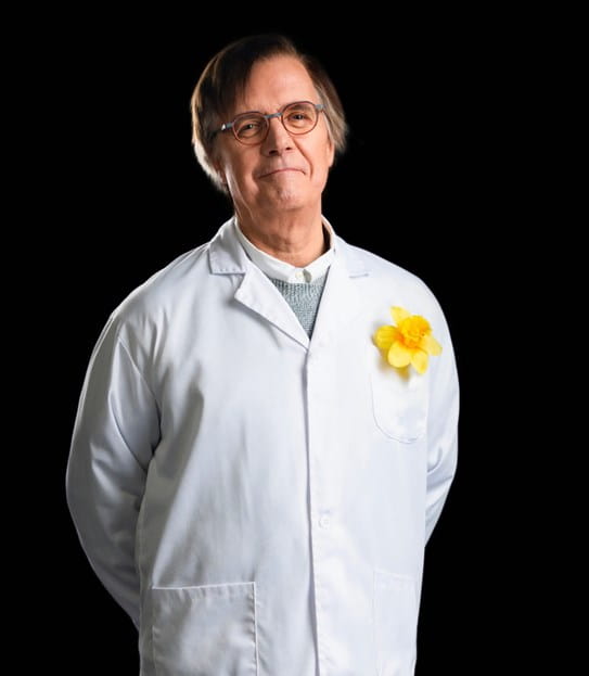 Dr Claude Perreault smiling at the camera with his hands behind his back, wearing a lab coat and a daffodil pin.
