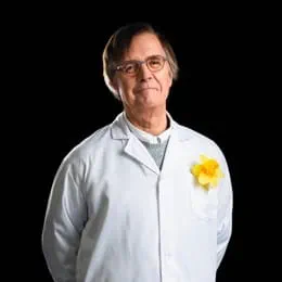 Le Dr Claude Perreault souriant devant l’appareil photo, les mains dans le dos, vêtu d’un sarrau arborant une épinglette jonquille.