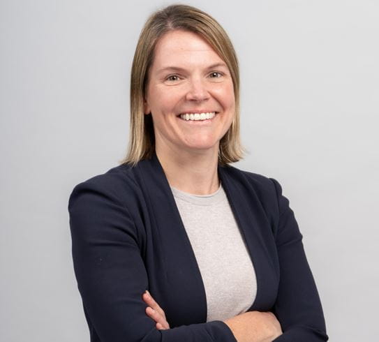 Dr Jennifer Croke smiling and standing in front of a wall with her arms crossed.