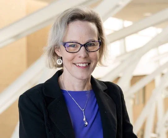 A headshot of Dr Linda Carlson, a researcher with fair hair, glasses and a black jacket over a blue shirt.