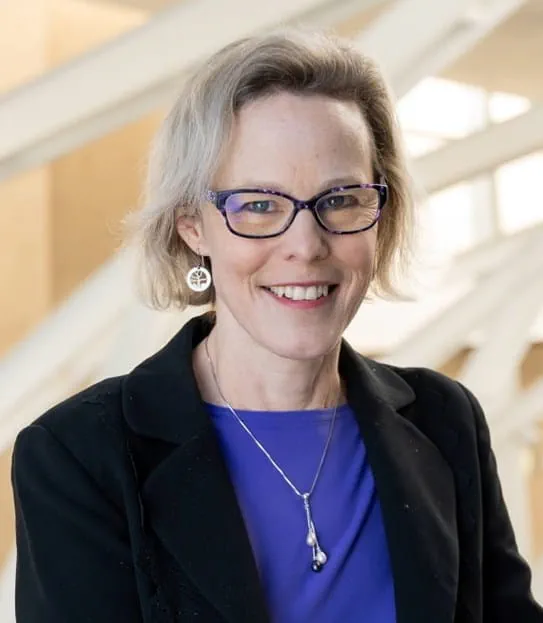 A headshot of Dr Linda Carlson, a researcher with fair hair, glasses and a black jacket over a blue shirt.