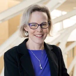 A headshot of Dr Linda Carlson, a researcher with fair hair, glasses and a black jacket over a blue shirt.
