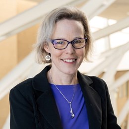 Photo du visage de la chercheuse Linda Carlson, Ph. D., cheveux blonds, lunettes et veston noir sur une chemise bleue.