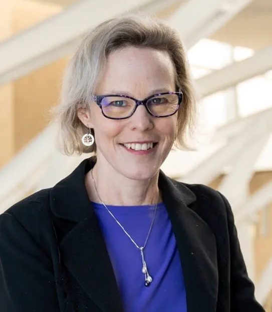 Photo du visage de la chercheuse Linda Carlson, Ph. D., cheveux blonds, lunettes et veston noir sur une chemise bleue.
