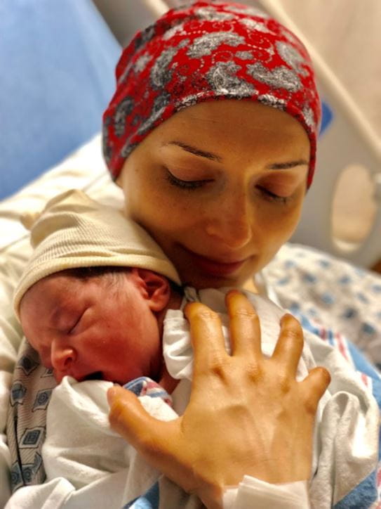 Salimeh wearing a headscarf and hospital gown in a hospital bed cradling her newborn son.