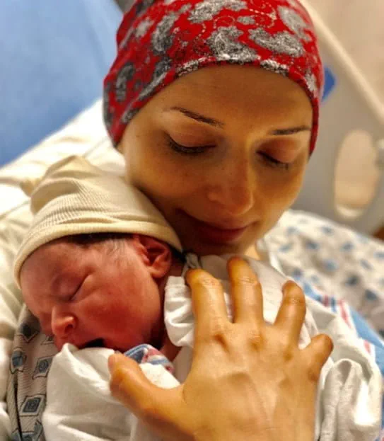 Salimeh wearing a headscarf and hospital gown in a hospital bed cradling her newborn son.