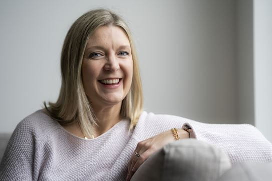 Kathy Andrews, souriant, assise sur un sofa.