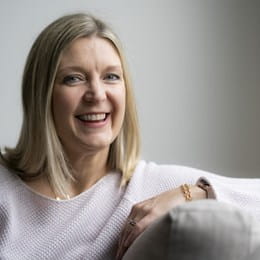 Kathy Andrews, souriant, assise sur un sofa.