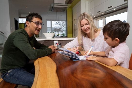 Kathy Andrews, en train de colorier avec son fils à la table, devant son partenaire souriant.