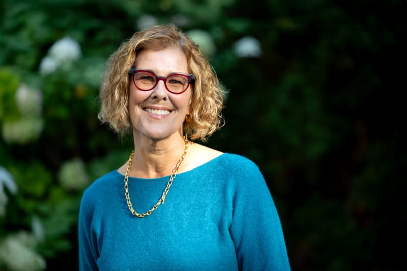 Bev Moir standing in front of trees and smiling.