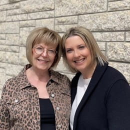 Karmen Schmidt and her mother standing in front of a brick wall and smiling.