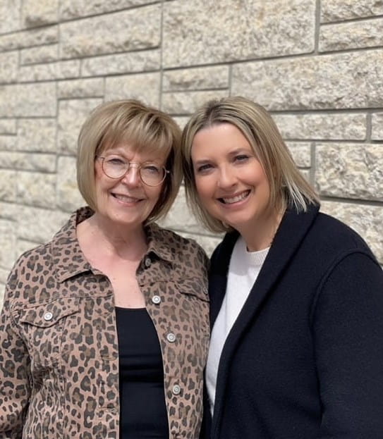 Karmen Schmidt and her mother standing in front of a brick wall and smiling.