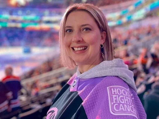 Karmen Schmidt souriant et se tenant dans un aréna, portant un chandail Le hockey pour vaincre le cancer.